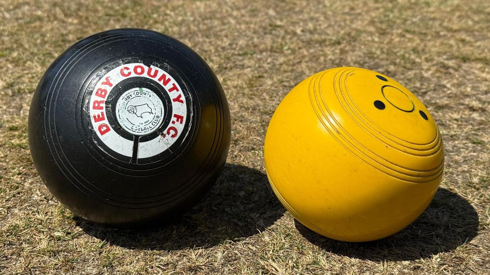 A black wood bearing the words DERBY COUNTY FC and a Rams logo and a yellow jack resting on a lawn