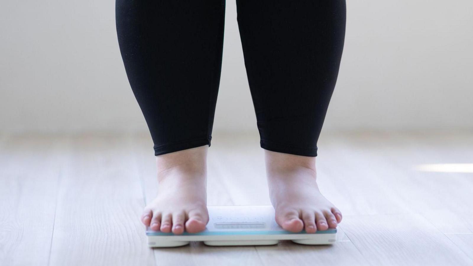 An anonymous woman who is overweight stands on some weighing scales
