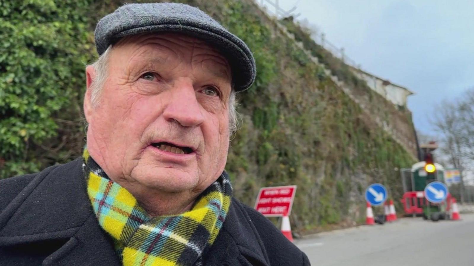 Smiling older man wearing a flat cap and a Cornish tartan scarf. 