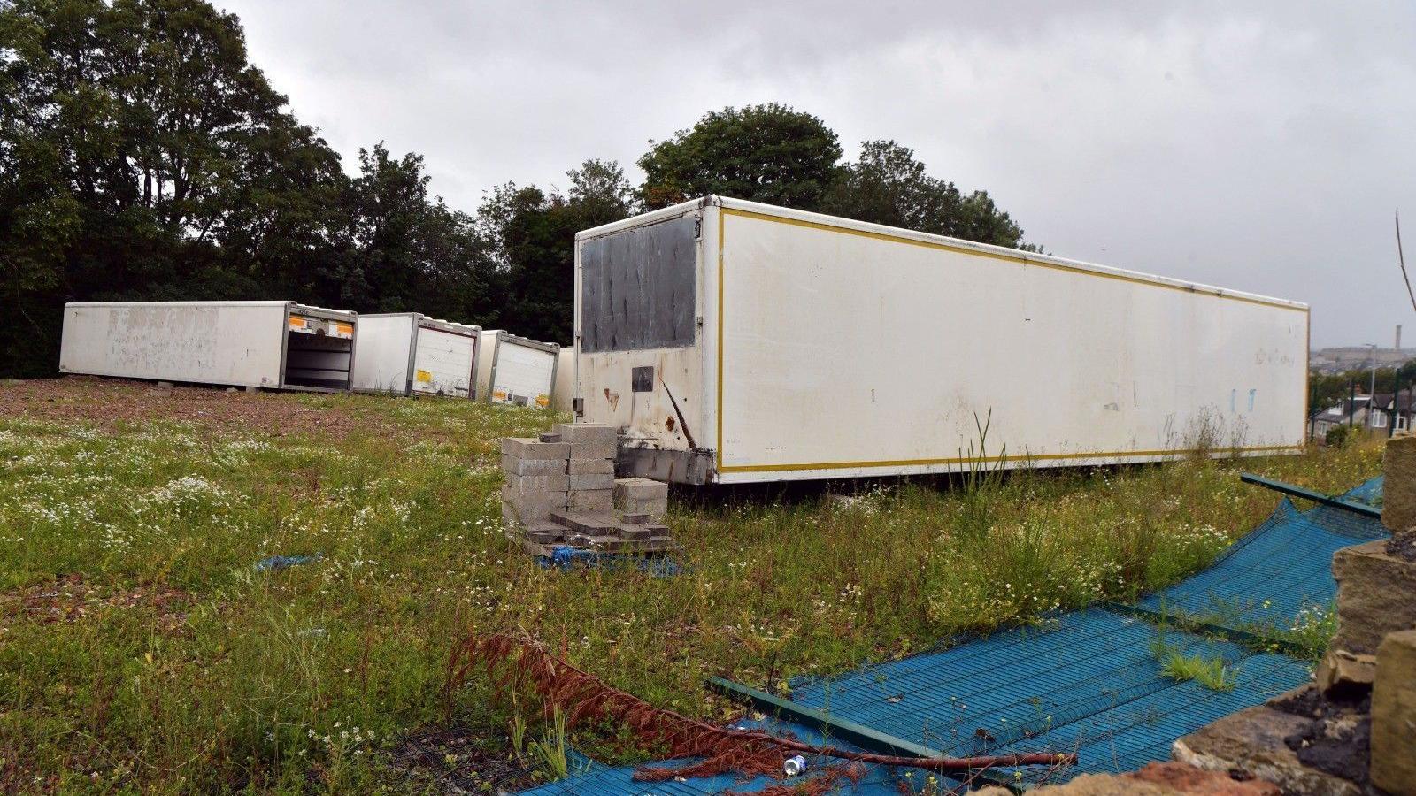 Large, white storage containers and cement blocks in a messy field