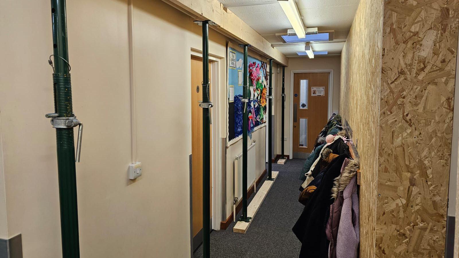 A hallway with pupils coats is lined with vertical props and wooden ceiling beams