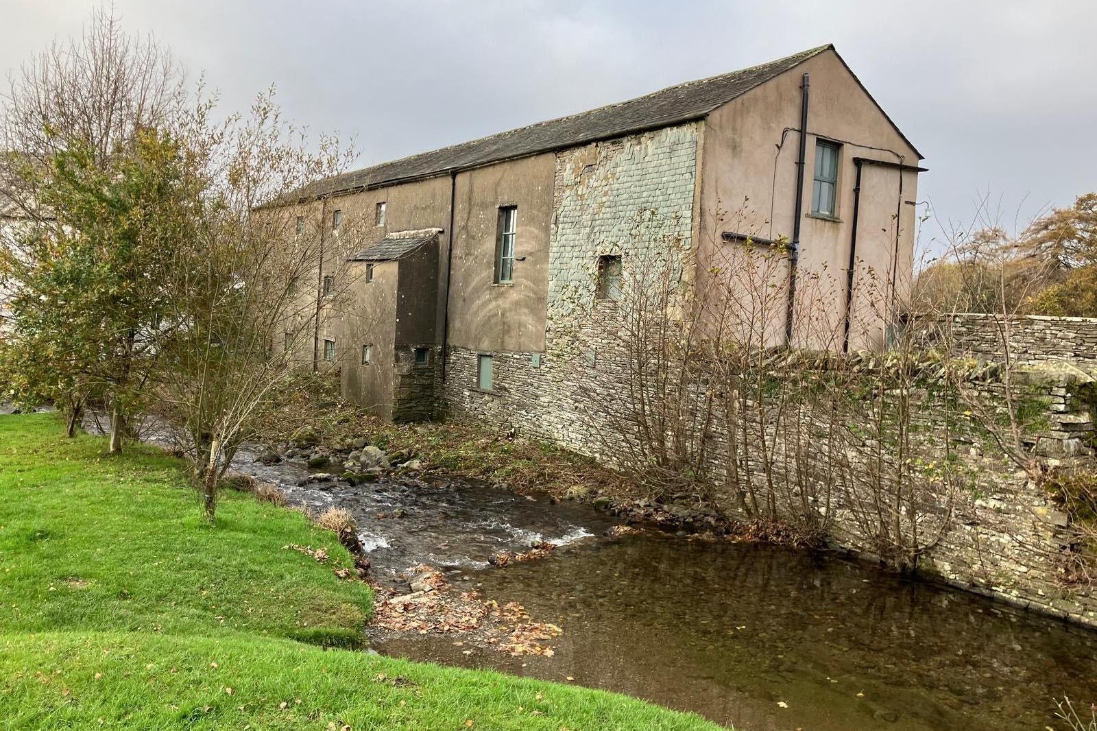 Yew Tree Hall is a three-storey building, with a black slate roof, in a state of disrepair. A beck flows beside it.