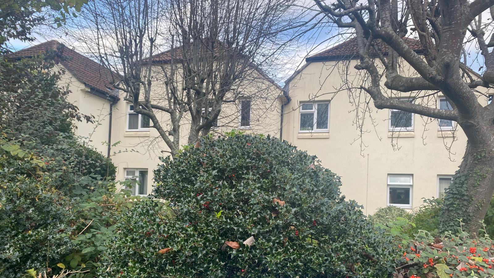 A block of flats in Westbury-on-Trym. They are cream with dark brown roofs. There is a hedge in front of the block.