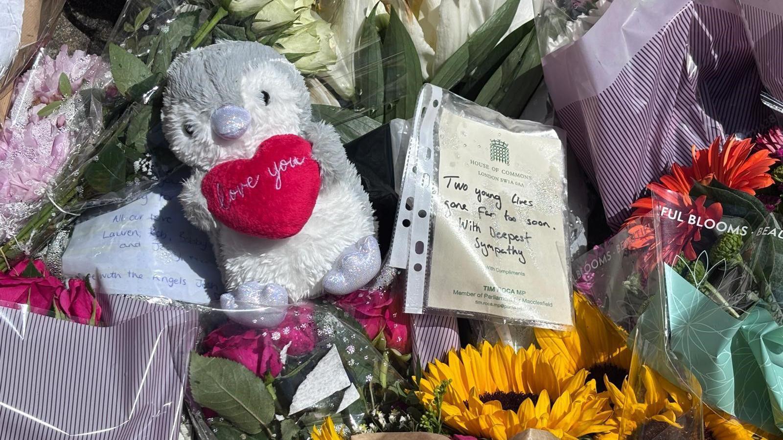 A number of bunches of flowers, a stuffed penguin and handwritten notes are on the ground.
