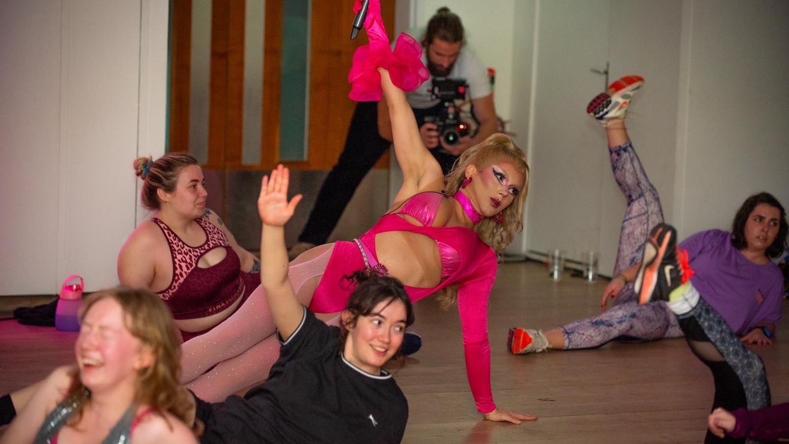 Ms Wailer wearing pink tights and pink outfit leading a workout class with other women holding their legs in the air. 