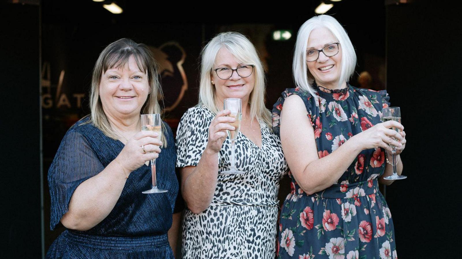 Kathy, Sarah and Debbie all holding a glass of champagne, smiling at the camera