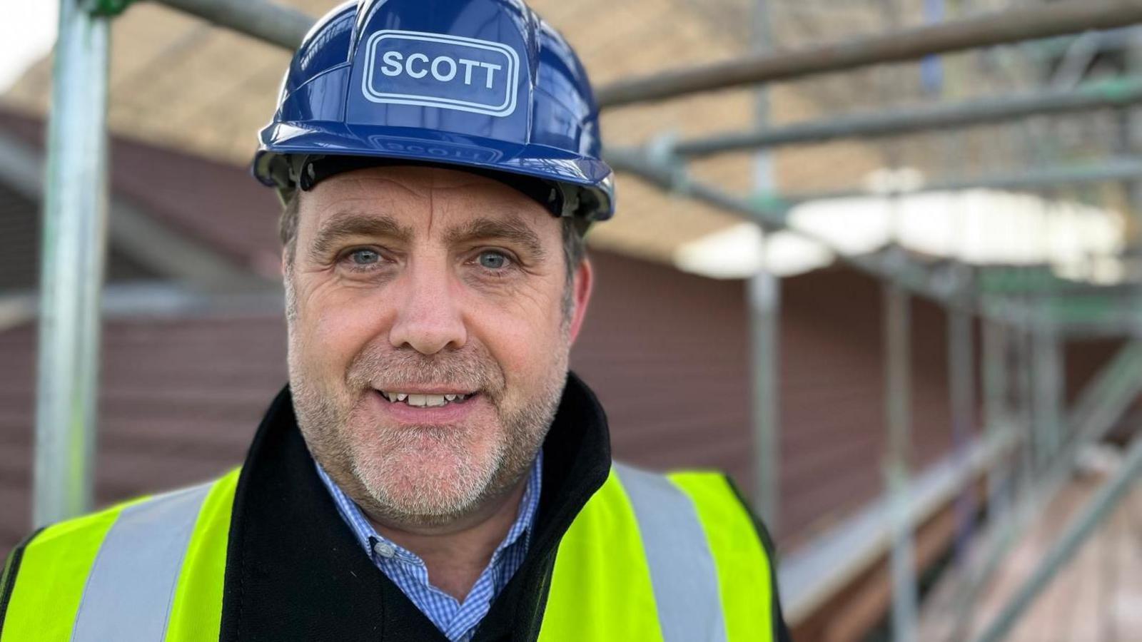 Paul Mears chief executive of the health board in a blue hard hat and yellow high-vis jacket at the site of the hospital roof repairs