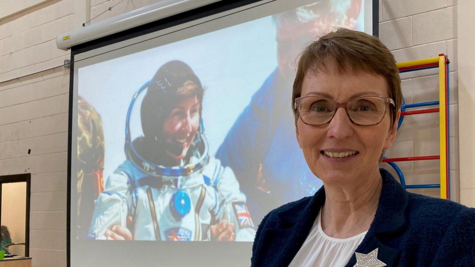 Astronaut Helen Sharman in front of a photo of her in space 