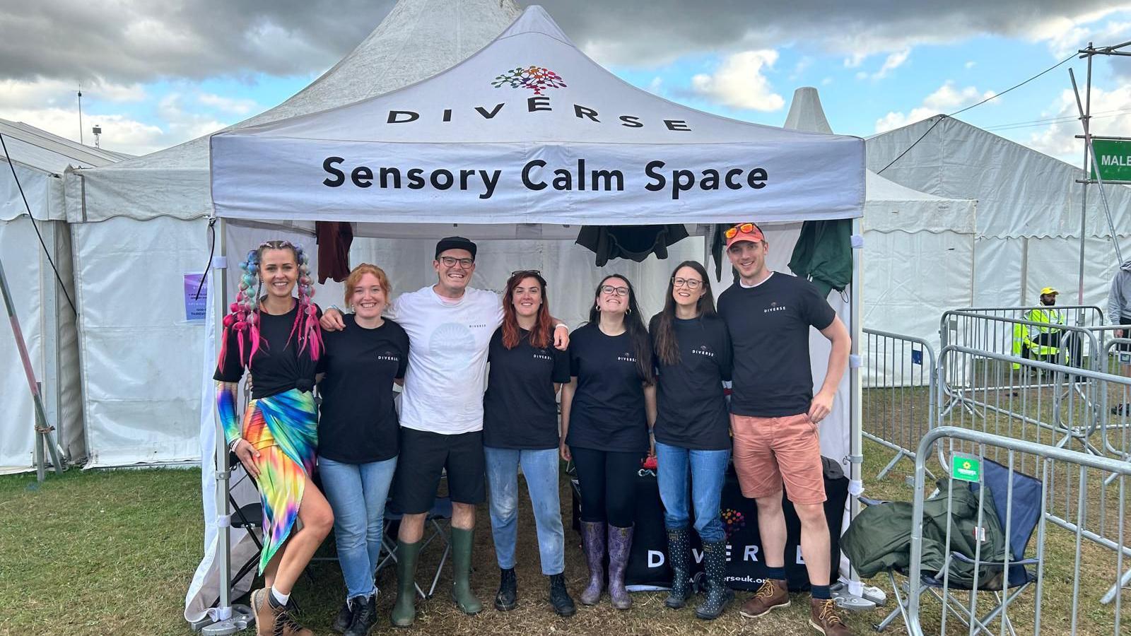 A group of people standing underneath a white tent which says sensory calm space. Behind them are white gazebos.