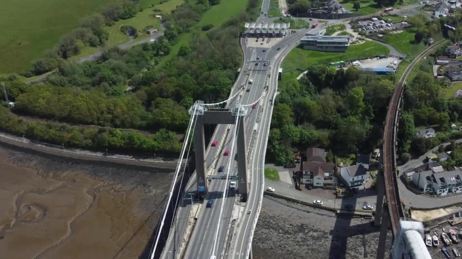 Bird's eye view of the Tamar bridge with toll booths at one end and several vehicles travelling along it.