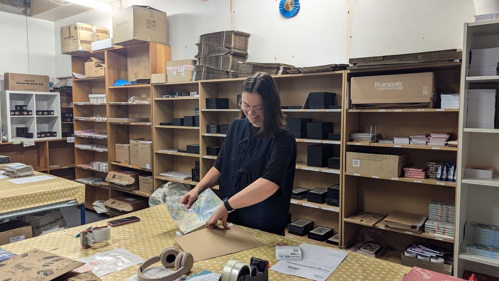 A woman in a back room surrounded by shelves packing a poster into a big brown envelope