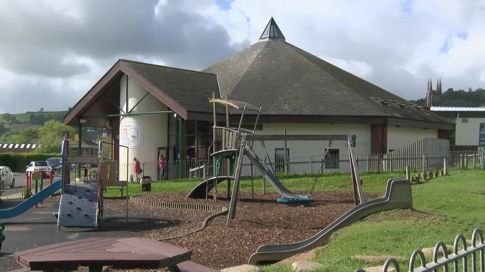 Totnes leisure centre. A circular building which looks like a church. A children's play area is in the foreground. 