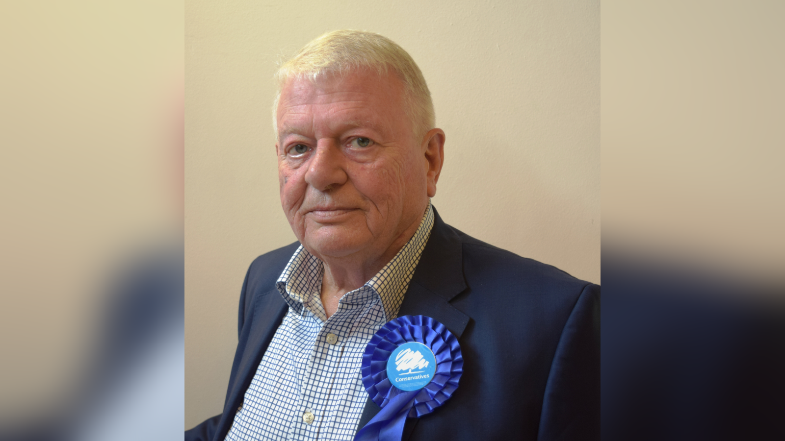 An elderly-man with a blue rosette on the lapel of his suit jacket.