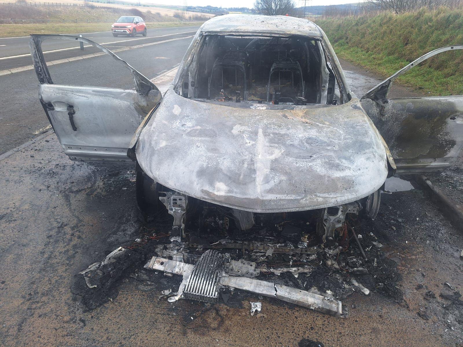 Pamje nga përpara e makinës së bardhë të dëmtuar plotësisht nga zjarri. Të gjitha dritaret janë hequr dhe ka mbeturina përreth automjetit.