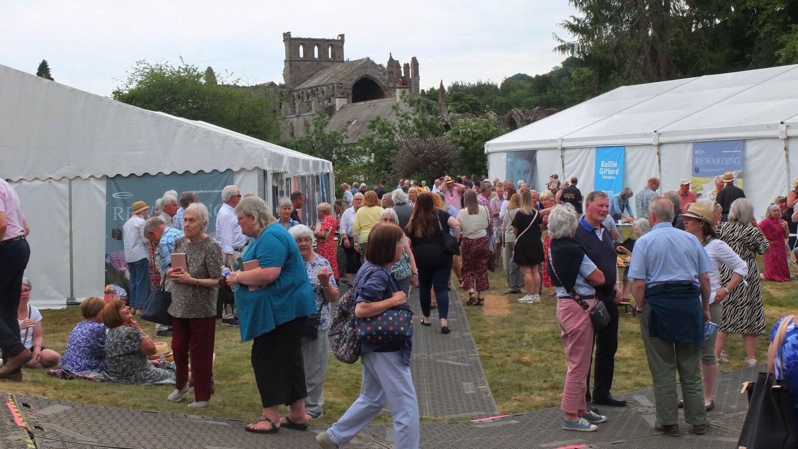 A busy book festival in Melrose with marquees and lots of people in the foreground and the town's abbey in the background