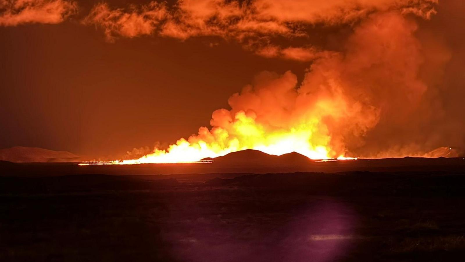 Fire appearing behind a mountain in the darkness, lighting the sky red and yellow