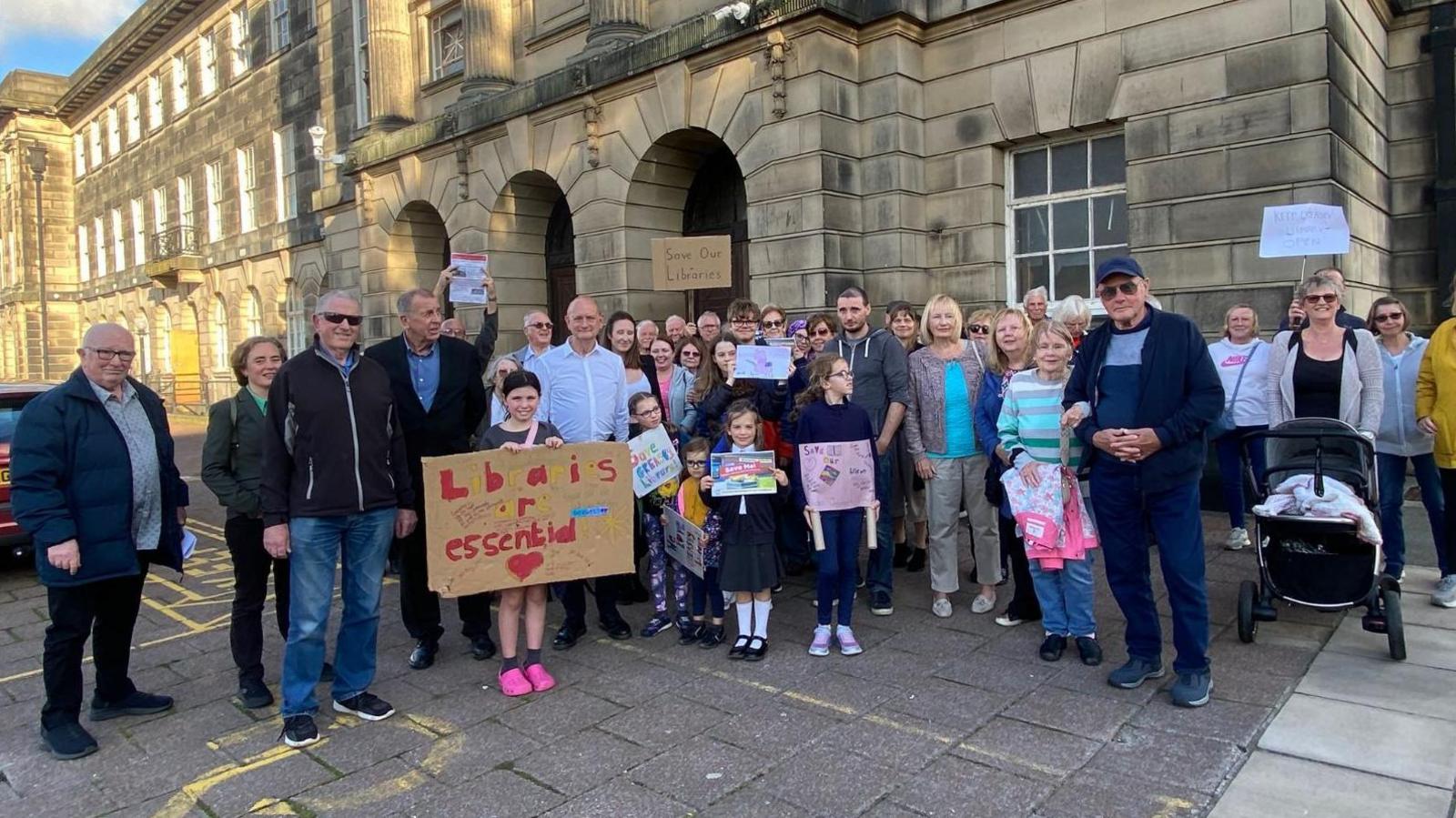 A group of people outside Wallasey Town Hall holding placards which read: 'Save Our Libraries' and 'Libraries are essential'.