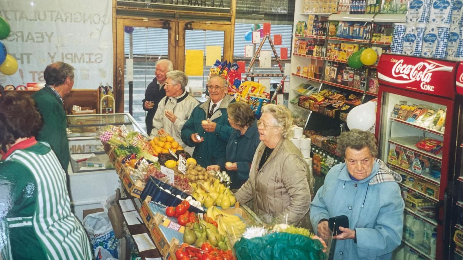 A picture from the 1980'S of a busy fruit and veg store. Customers line up to be served.