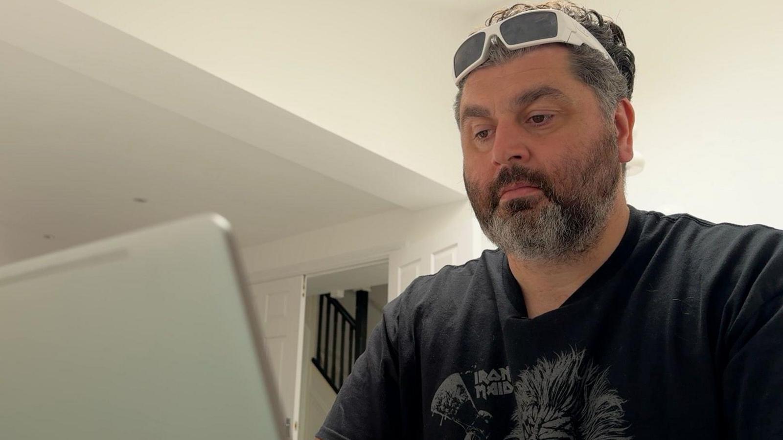 Oliver Moazzezi is sat looking at his computer screen. He has a beard, white glasses on his head and a black t-shirt.