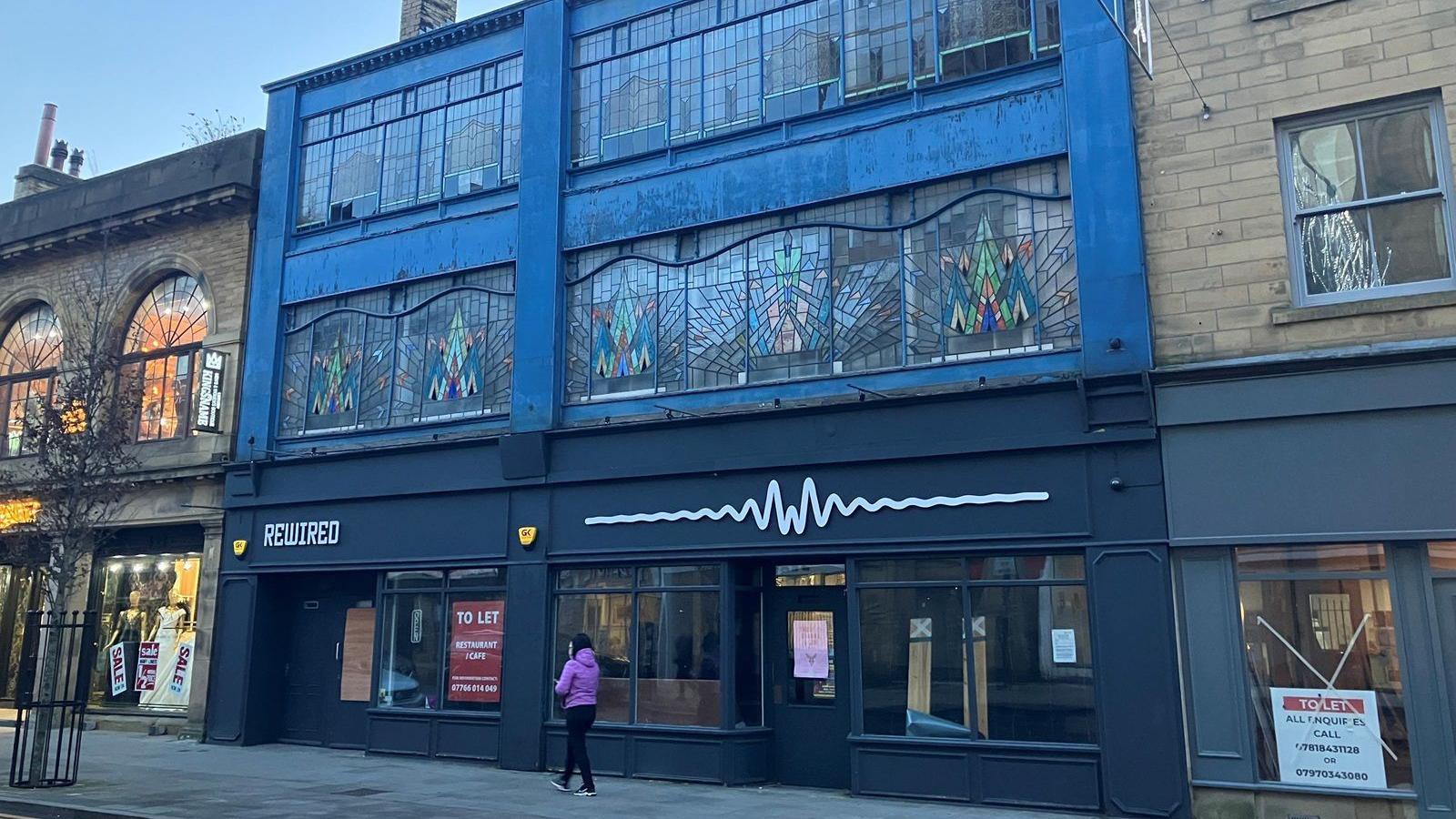 A photograph of the building shows the colourfully decorated windows stretching across the upper floor. An empty unit below has a "to let" poster fixed to the window.