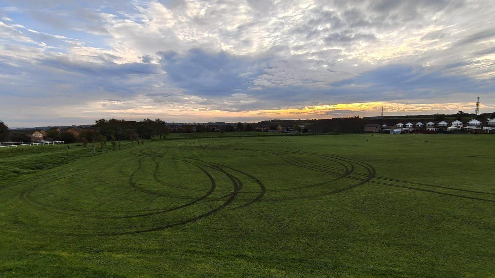 A football pitch with tyre tracks at sunrise, with lots of clouds in the sky.