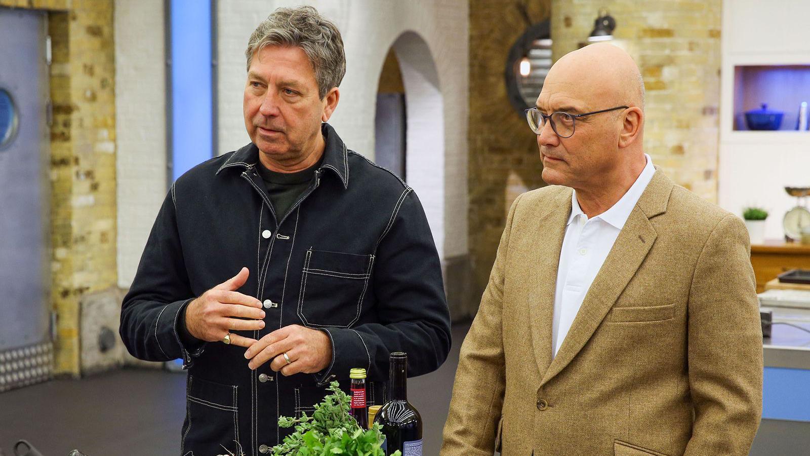 John Torode, left, and Gregg Wallace standing in the studio kitchen. Torode is wearing a black shirt with white rims. Wallace is wearing a brown or cream coloured jacket.