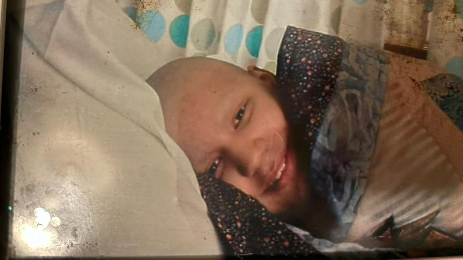 An old photo of a young teenage boy smiling from a hospital bed