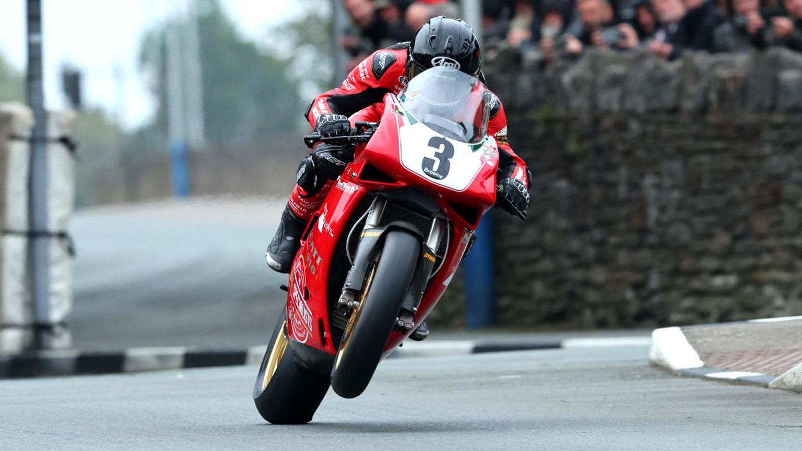 Mike Browne racing on a red motorcycle with a white plate with the number the written in black on it on the front. He's wearing red and black leathers and a black helmet.