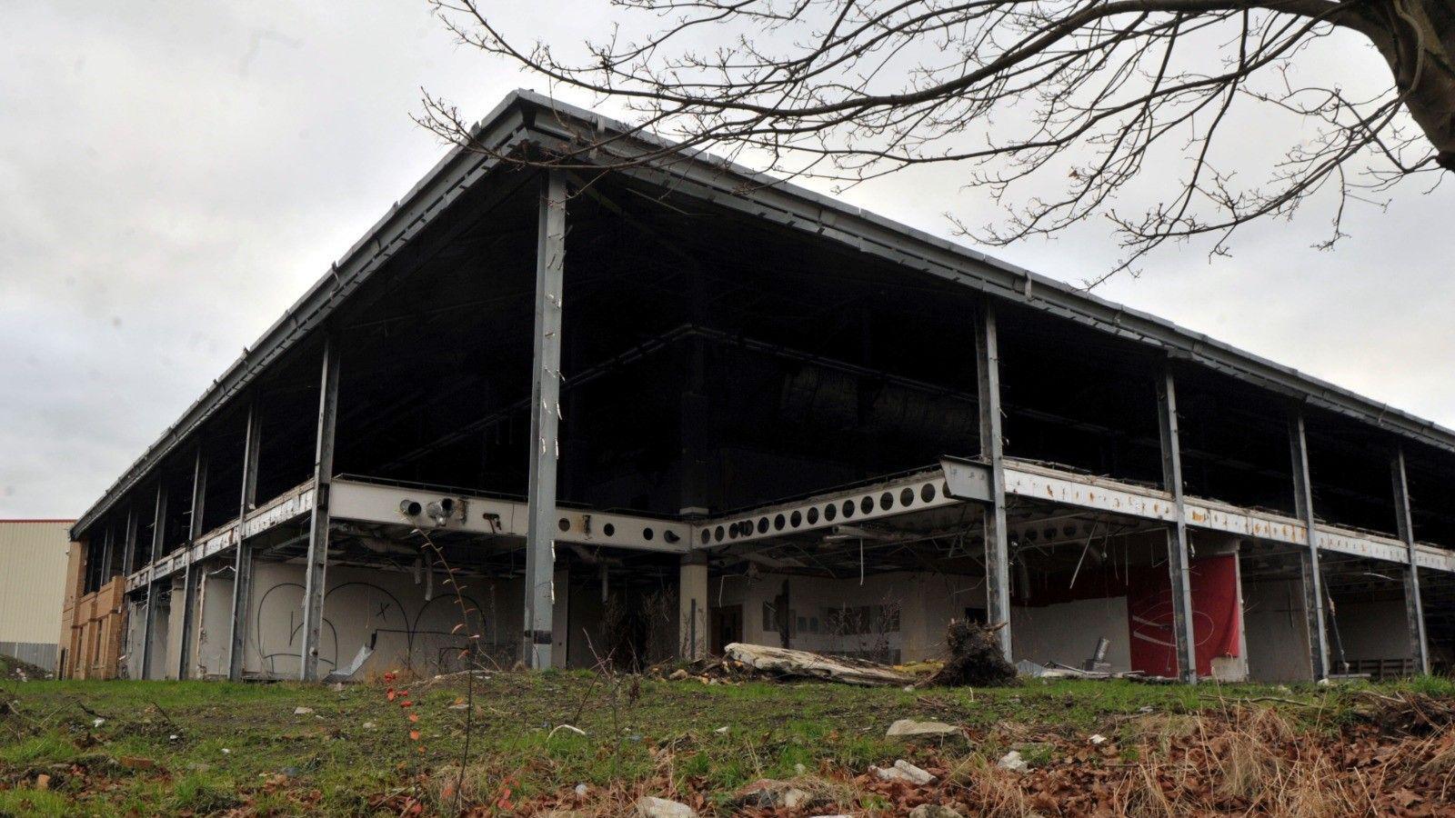 A derelict building in Bradford, with no walls still intact. The site has been stripped down to its steel frame.  A tree is in the foreground, with grass surrounding the building. 