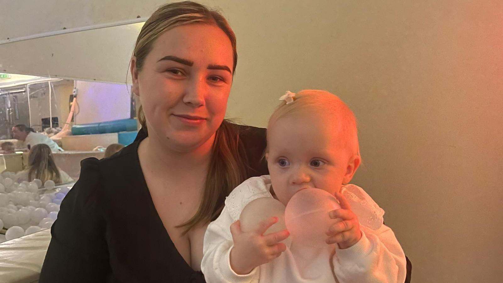 Kayleigh Brannan sits with her baby on her lap and the baby holds two plastic balls from a ball pit