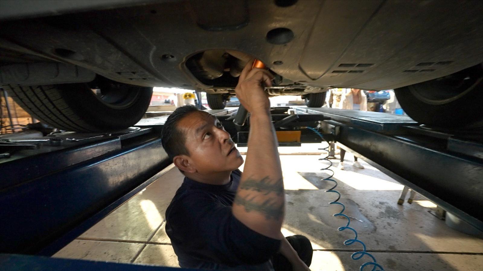 Jorge Gonzalez Jr uses a flashlight to look under a vehicle in an automotive repair shop in Arizona. 