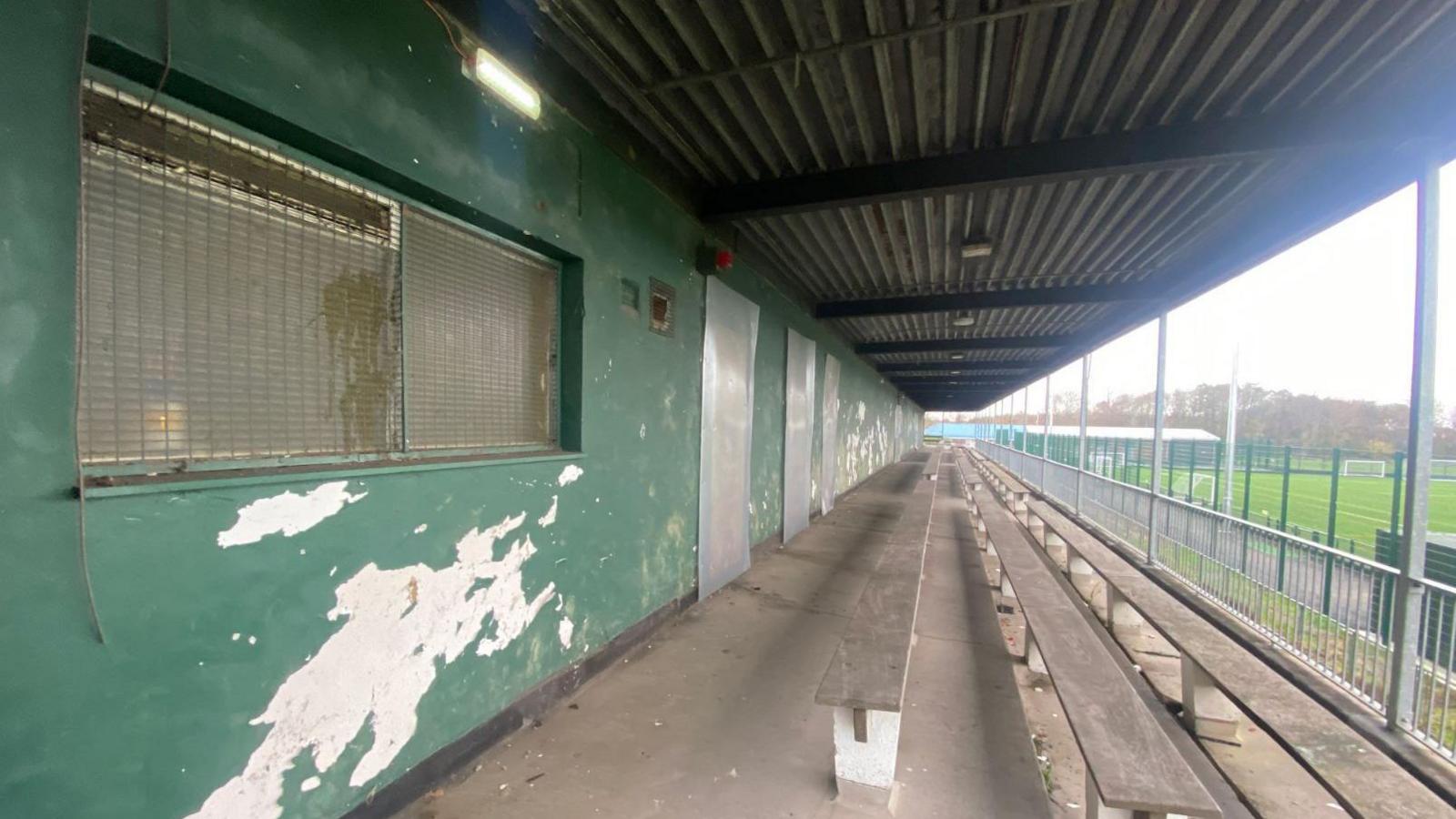 A derelict viewing terrace with wooden benches and metal grilles on windows and metal panels over doors.