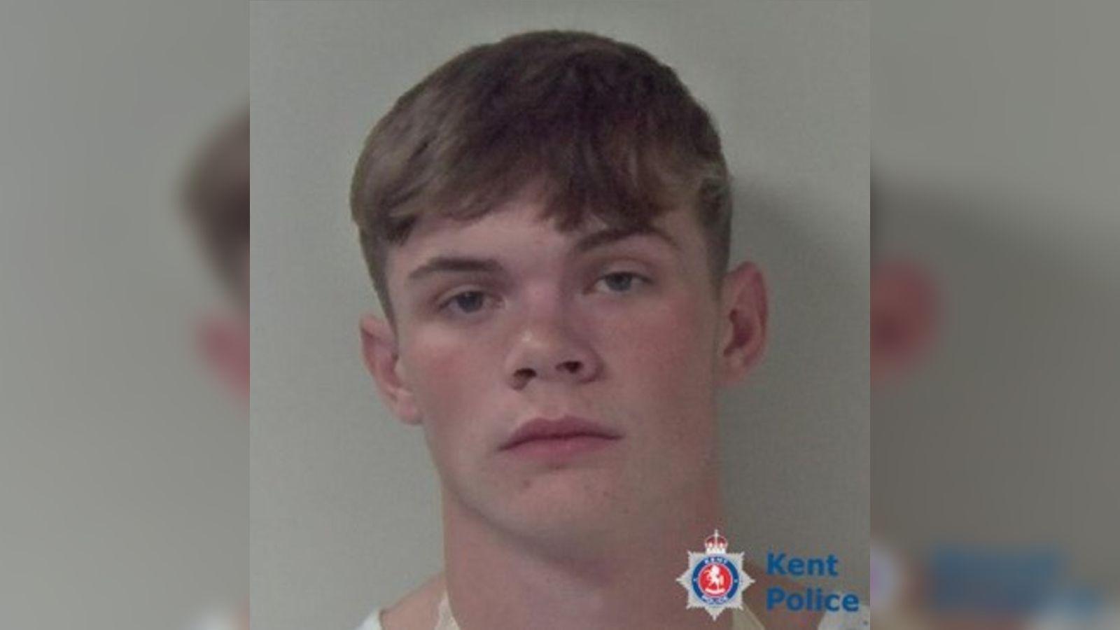 A young, clean-shaven man. His hair has a floppy fringe and short, shaven sides.