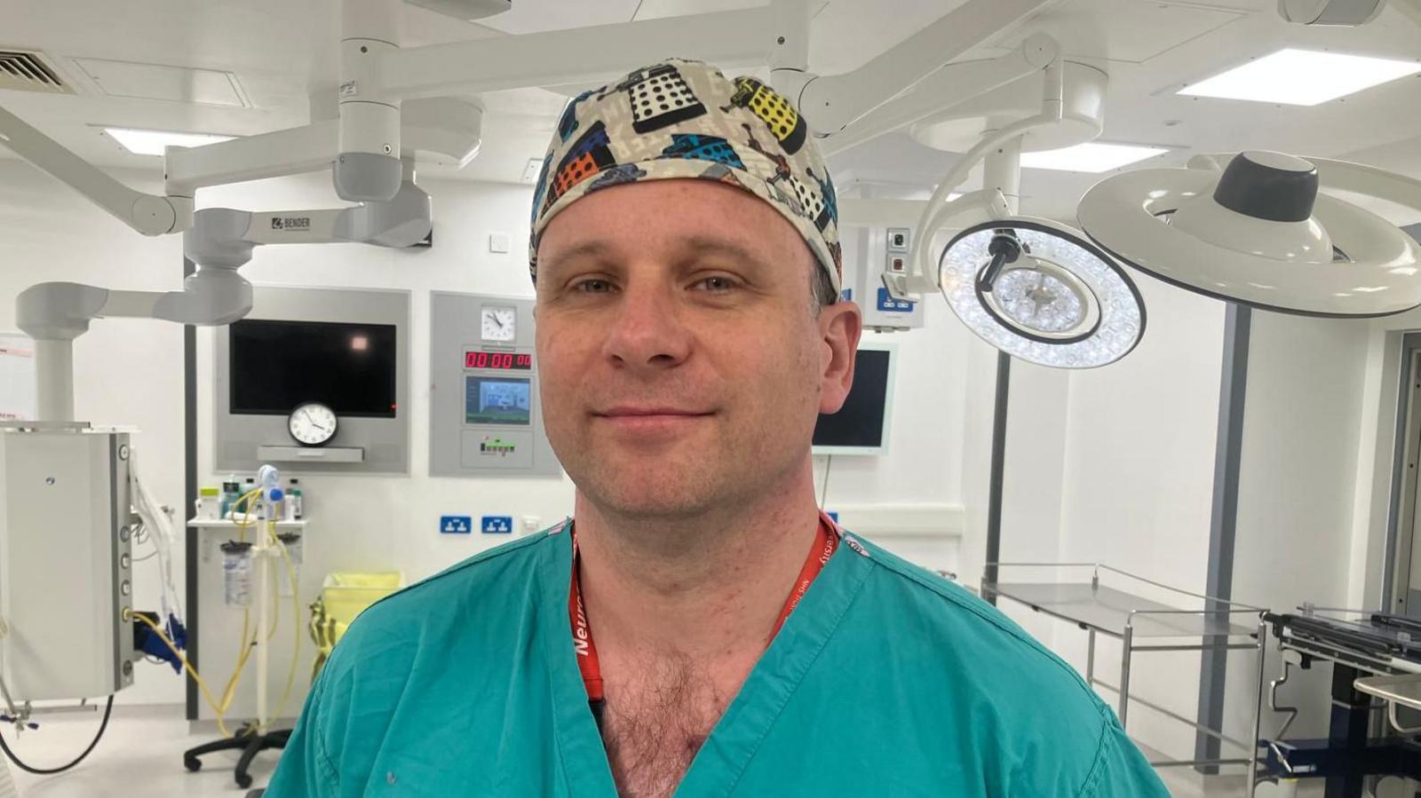 A man in green surgical scrubs and cap with daleks on it in an operating theatre