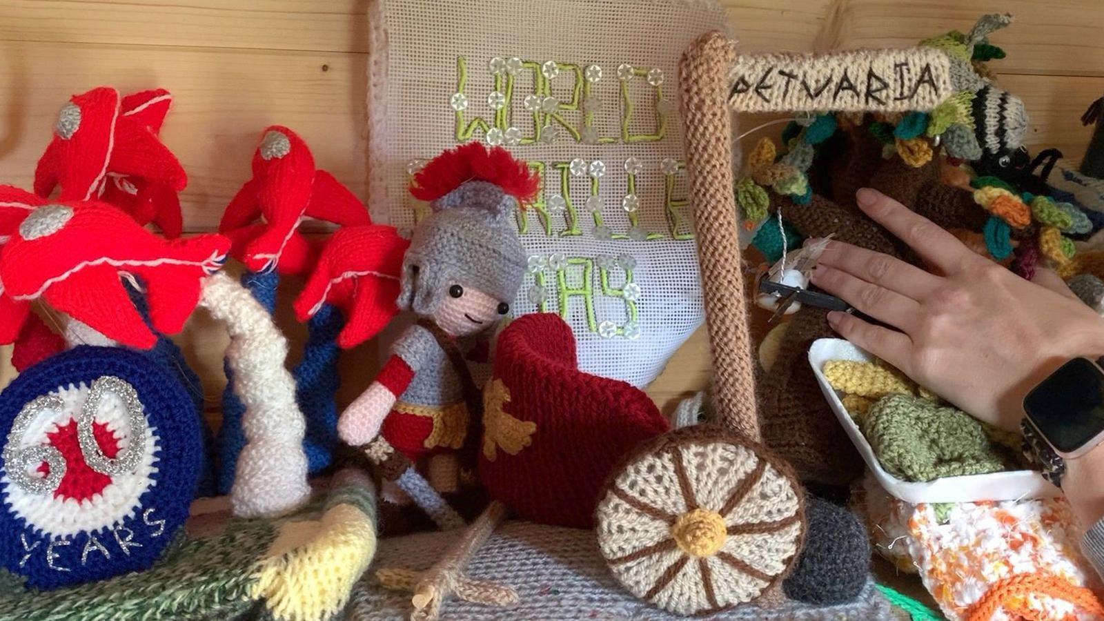 Knitted creations on a shelf inside the wooden shed. They include a Roman soldier, a cart wheel and a sign reading "Petuaria".