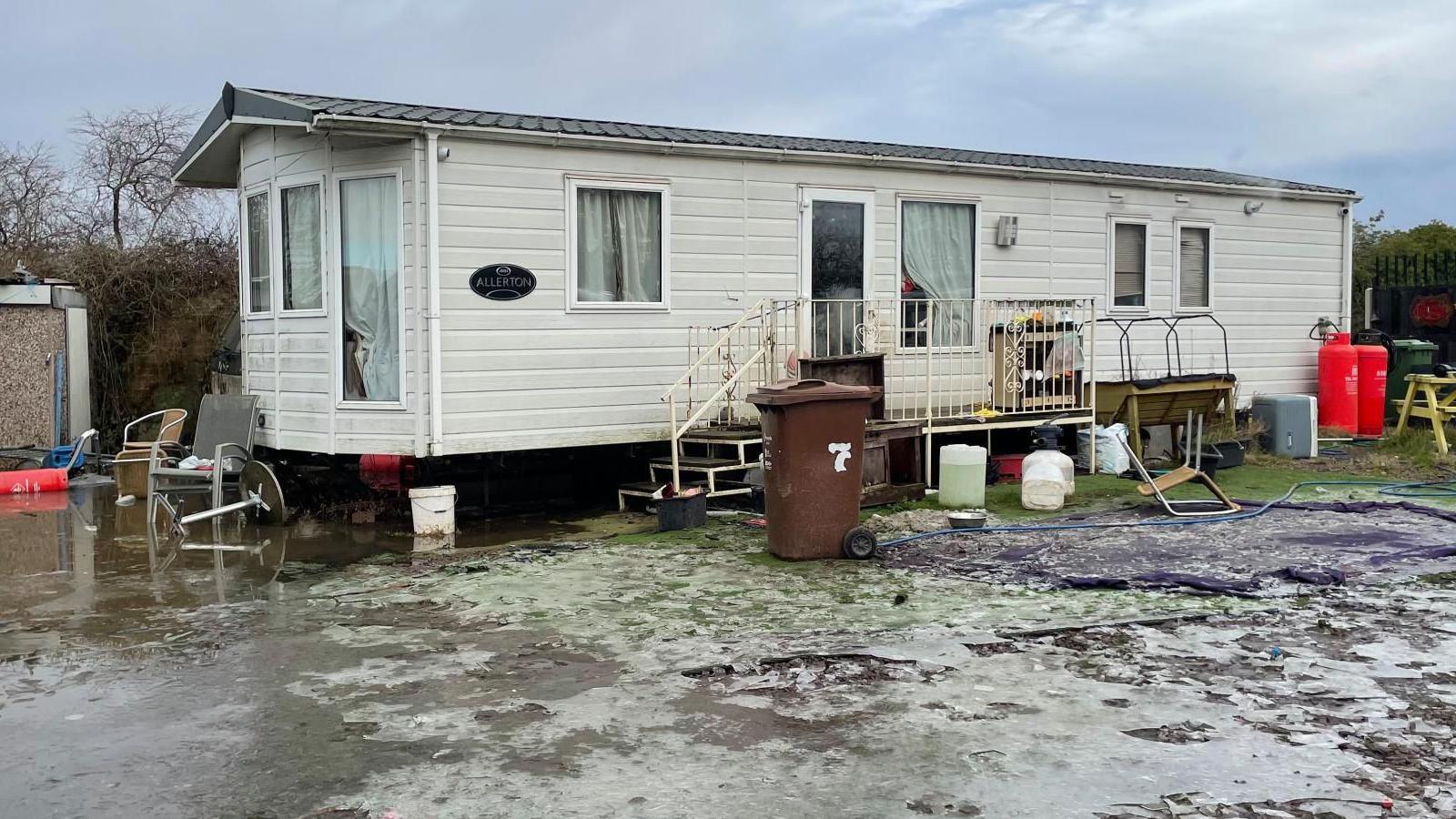 A static caravan stands surrounded by ice and flood water.