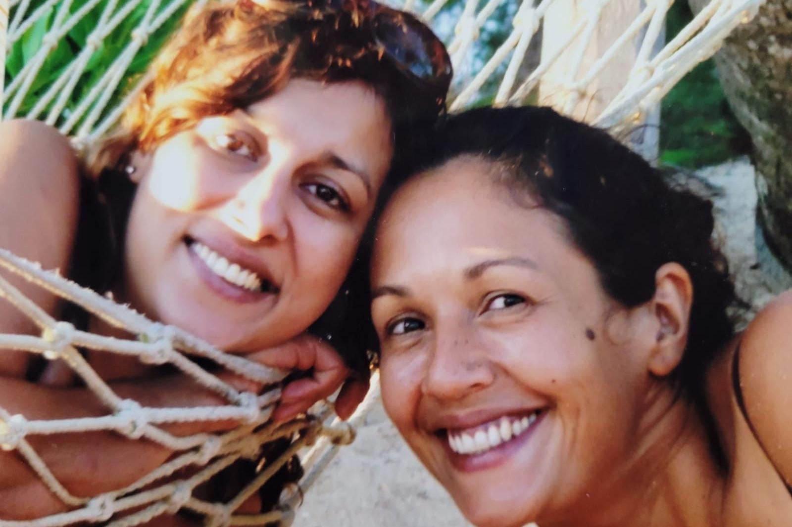 Ani Naqvi (left) and a friend smile while lying in a hammock, with sunlight and tropical greenery in the background.