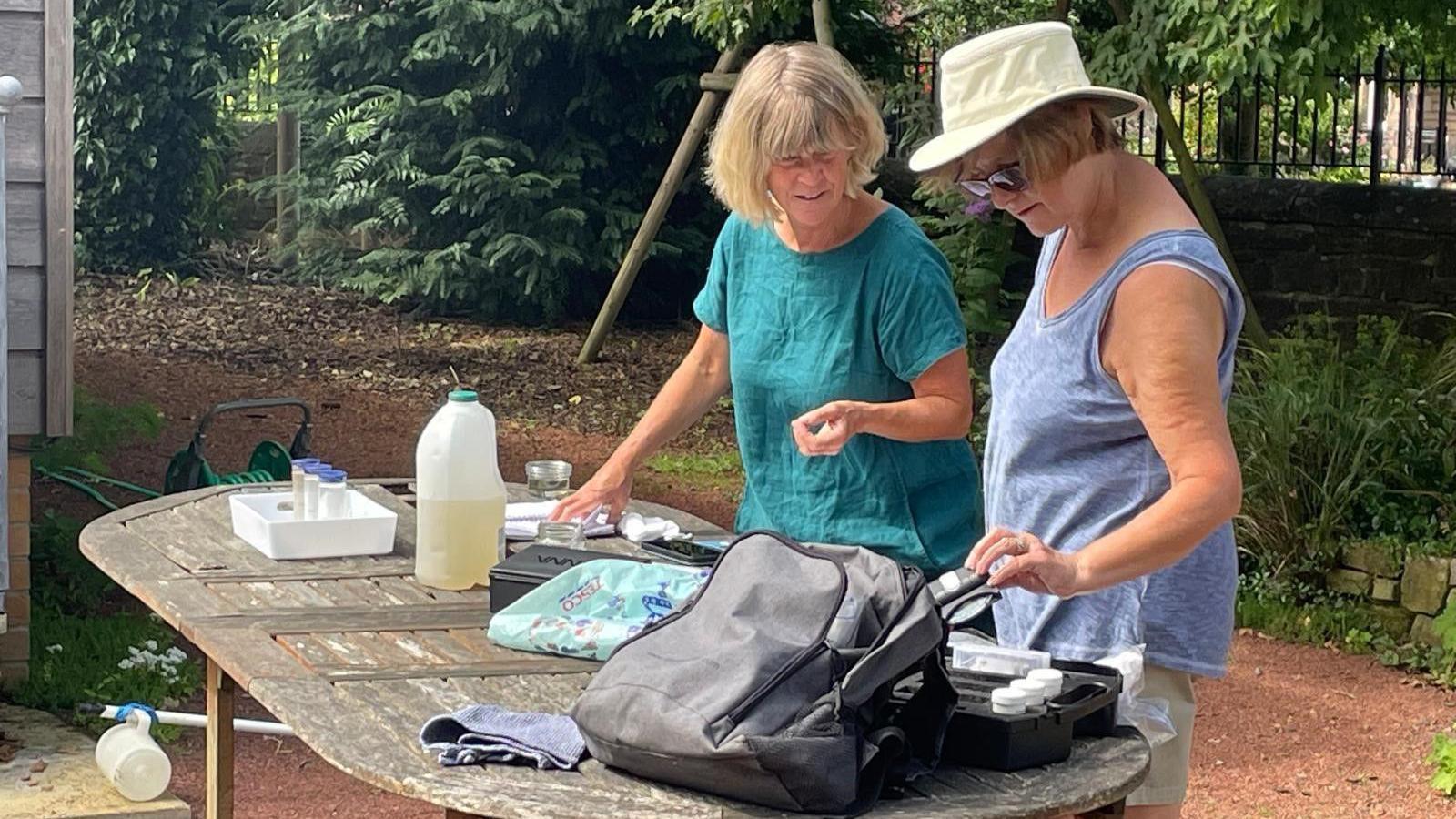 Two women in their sixties stand at a table on which there are various testing apparatus. They are talking together and discussing results 