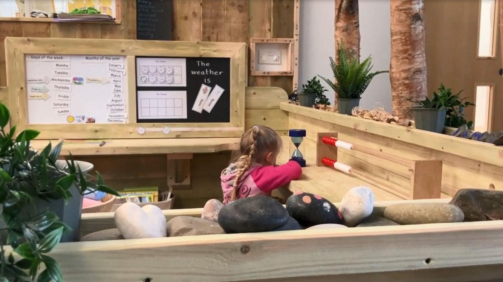 Child playing at wooden desk in classroom with trees and wooden benches