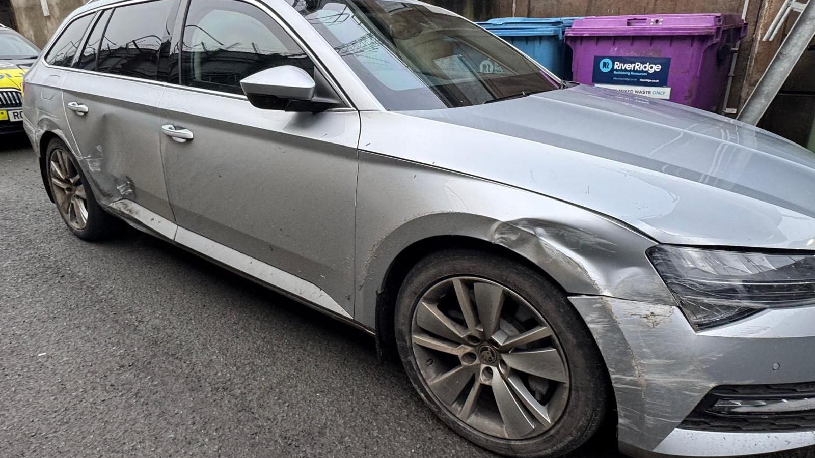 A silver Skoda Superb estate car, with visible dents and scratches along the side. 