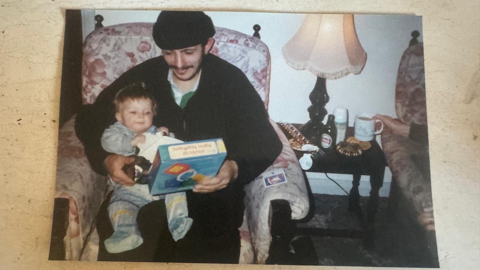 An old photo is shown of Omar holding a very young Mika on his lap holding a game box.