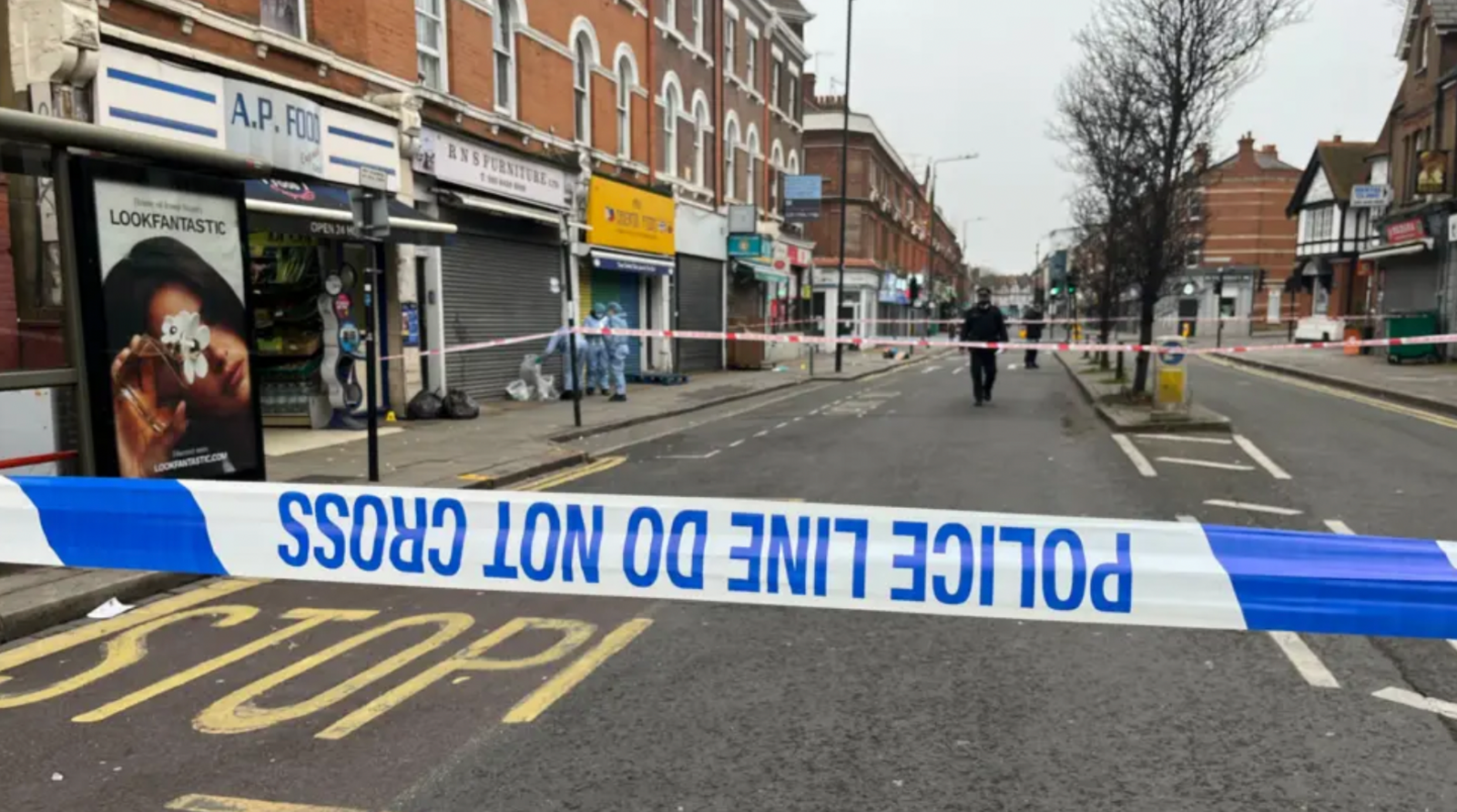 Police cordon tape on a London road. A police officer is seen in the distance.
