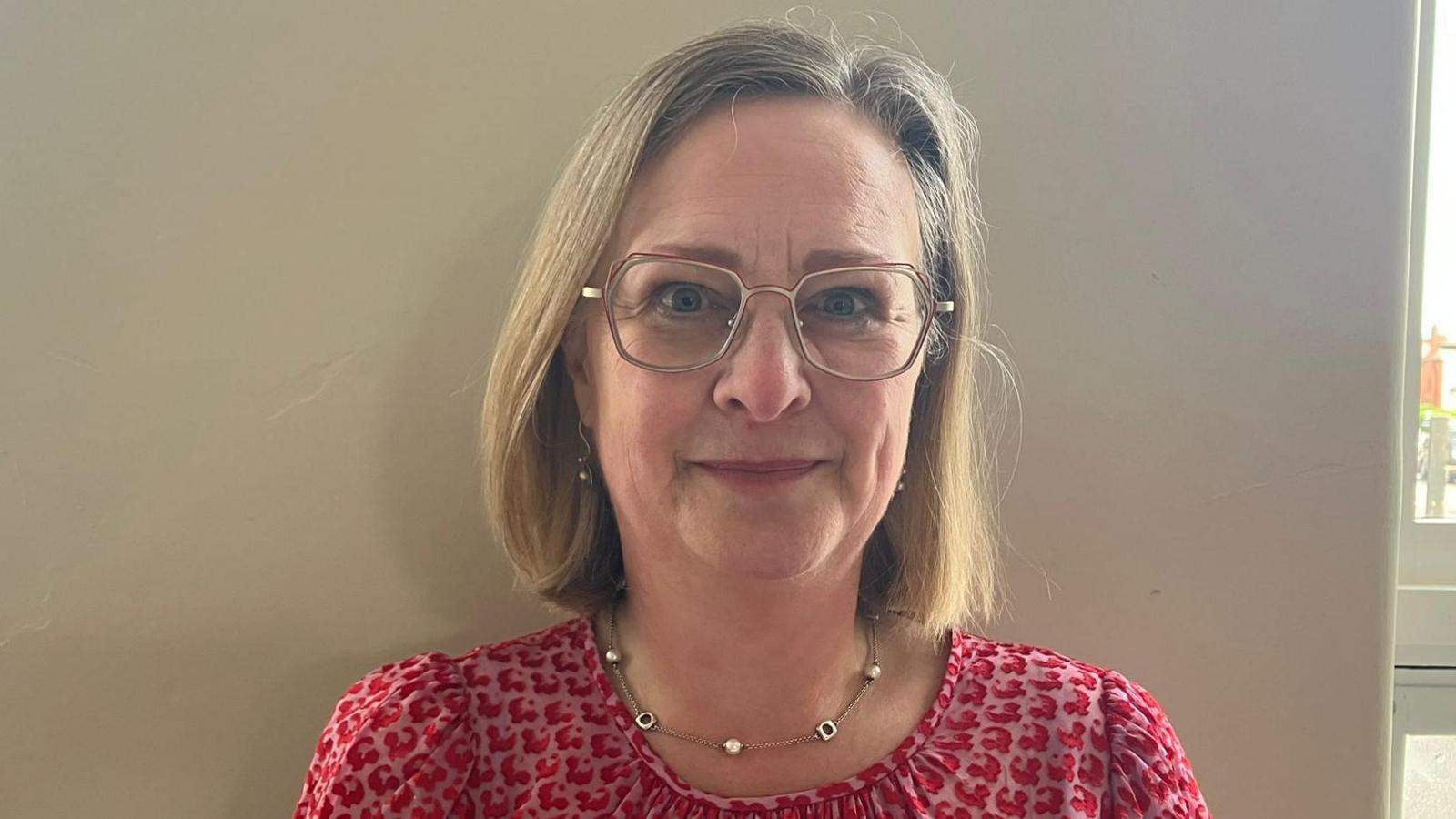 Thelma Crawford has short blonde hair and is wearing black and orange rimmed glasses.
