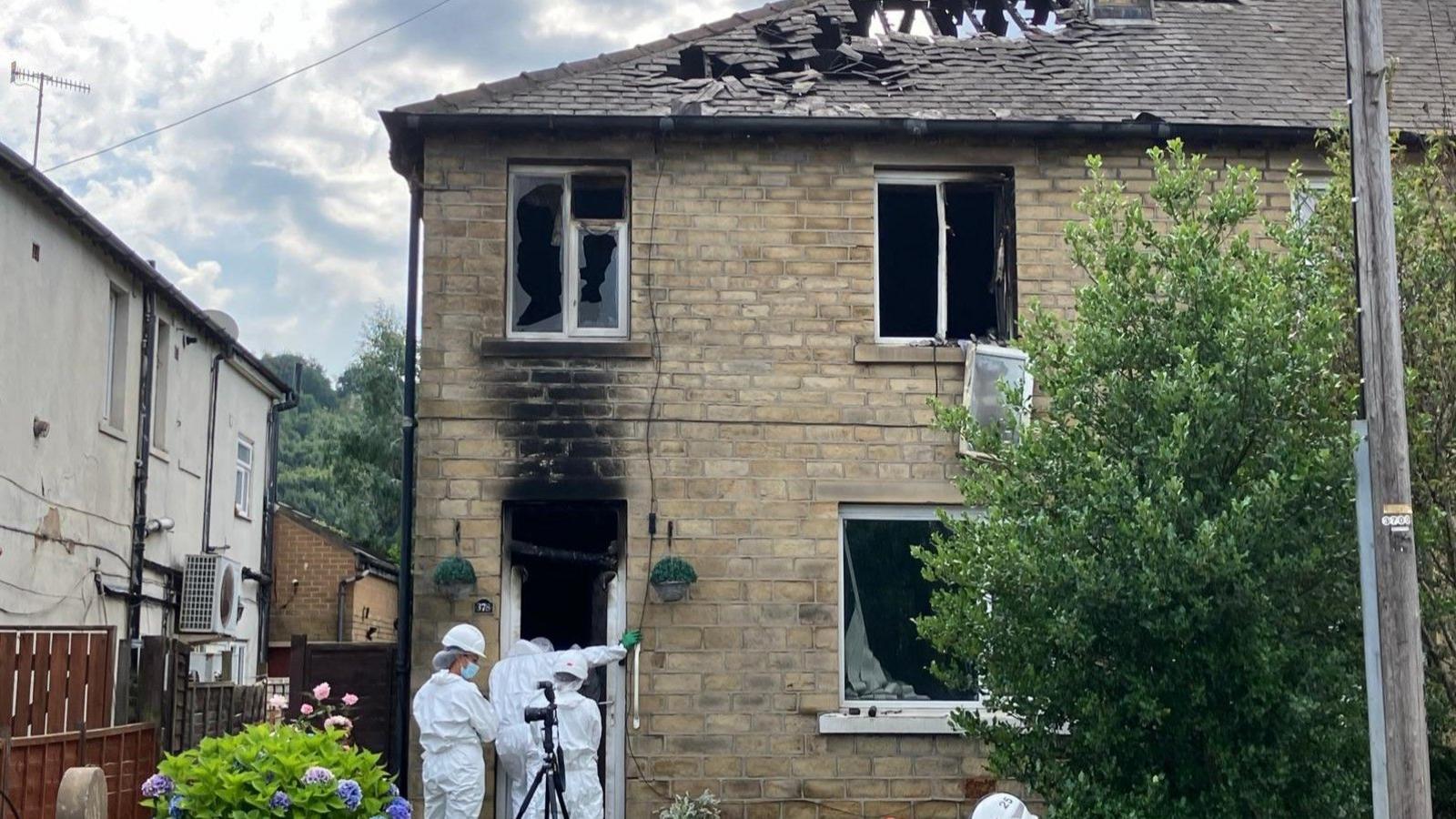 Forensic investigators in white suits stand in the front door of a burnt-out house