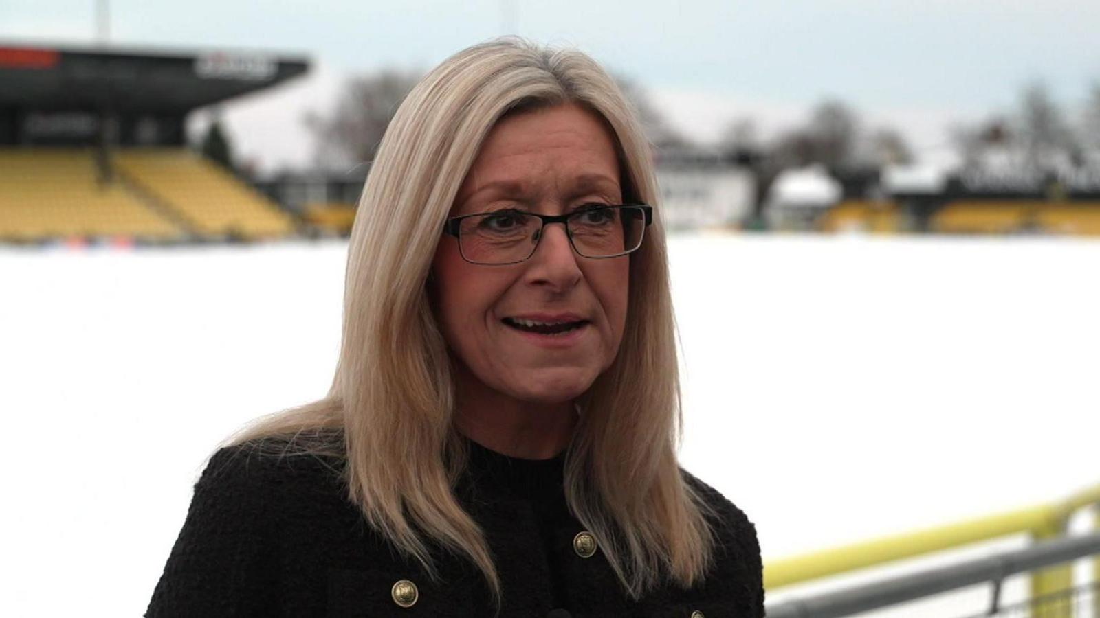 Sarah Barry wearing a black coat in front of a snow-covered football pitch.