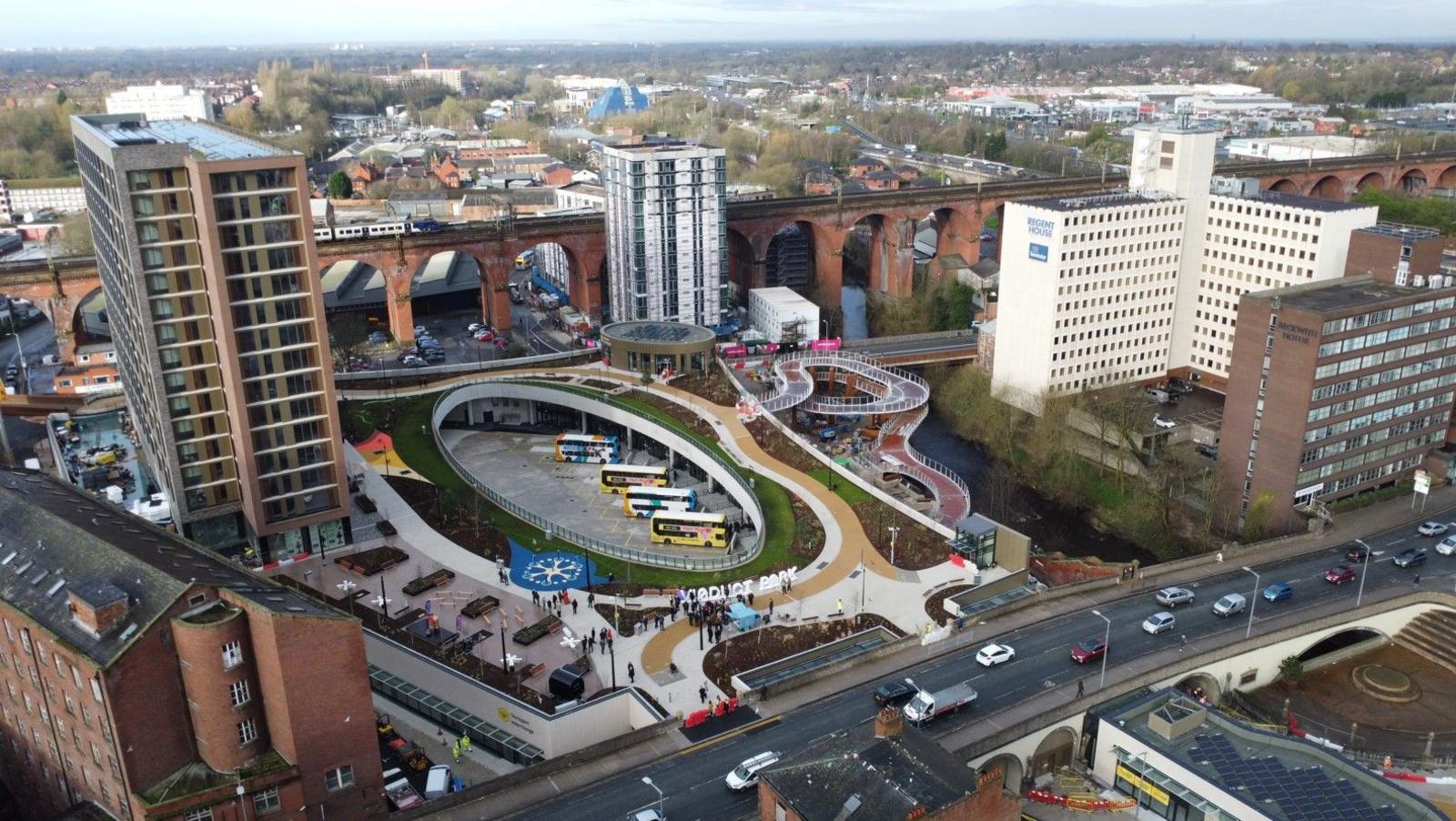 Drone shot of Stockport Interchange. There are many buildings including tower blocks. The main road looks very busy, with a stream of traffic.