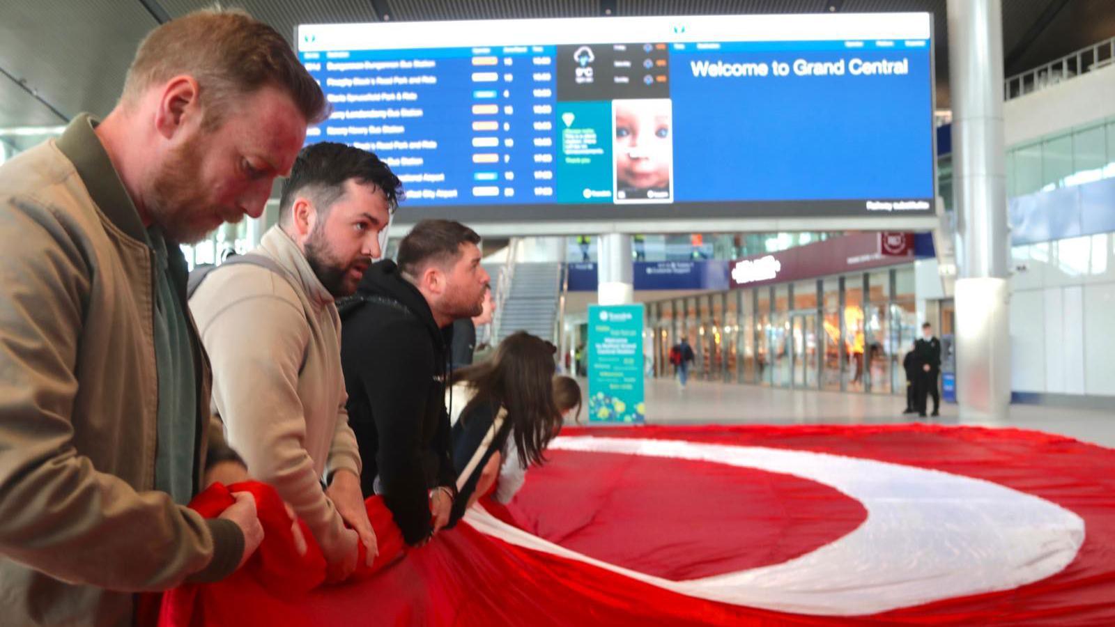 Irish language activists unfurling a red and white flag at Grand Central Station