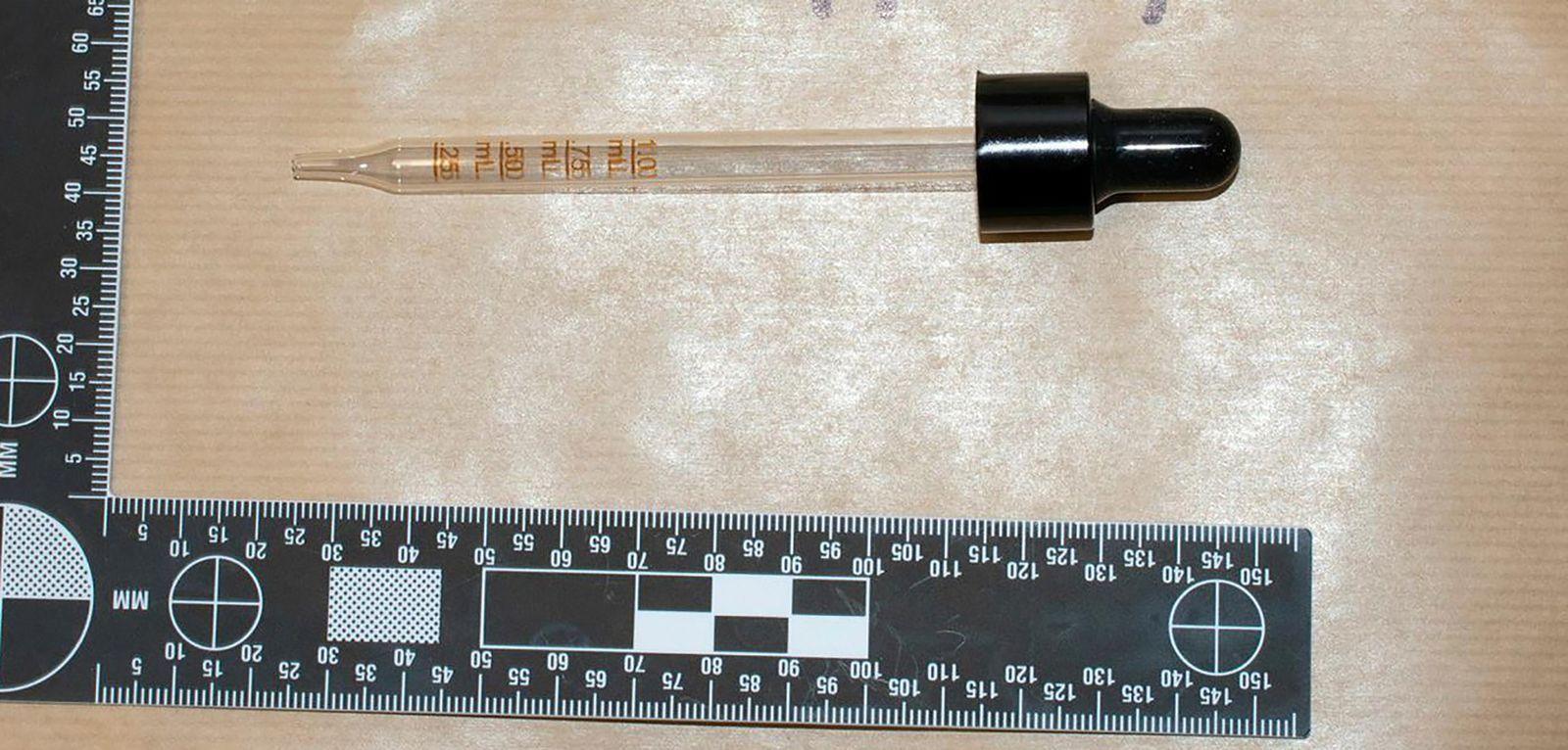 A clear pipette with measurements on it with a black top for dispensing liquid. A black and white ruler is pictured for scale