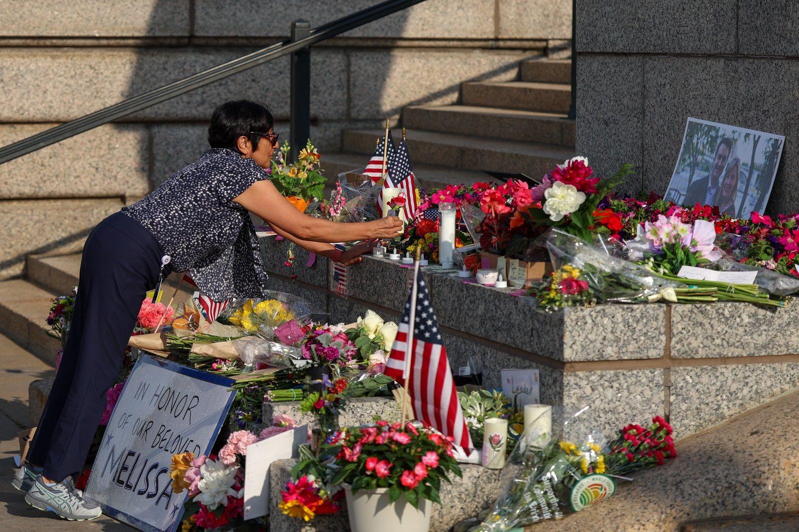 A display of flags and flowers fills the image as a woman leans over to lay a flower in the middle of the arrangement