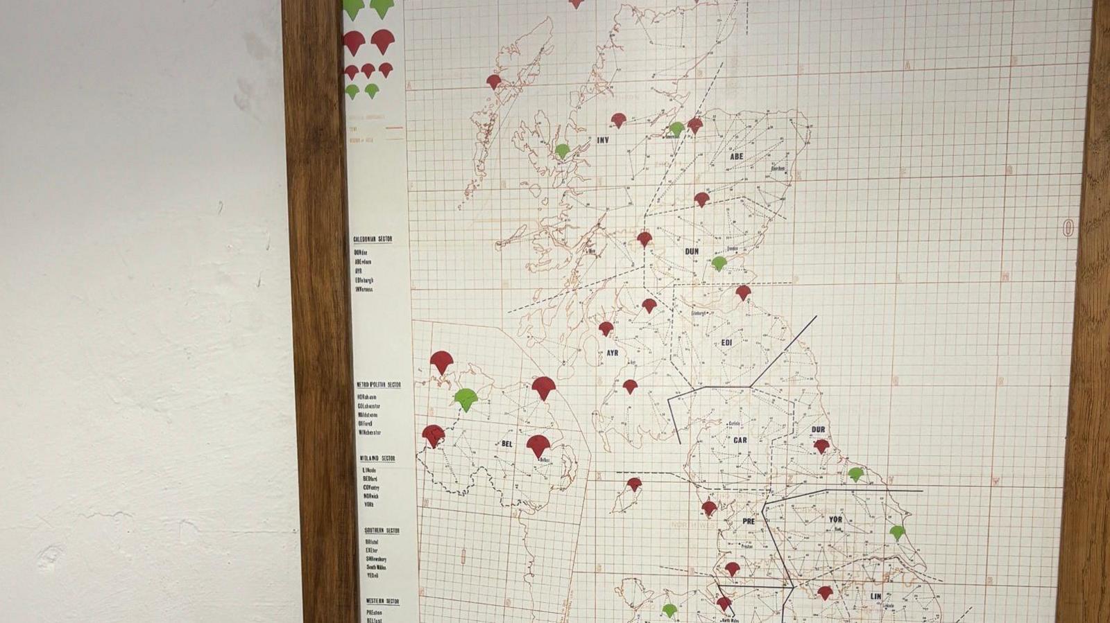 A map of the UK on a wall with red and green pins attached to various areas of it